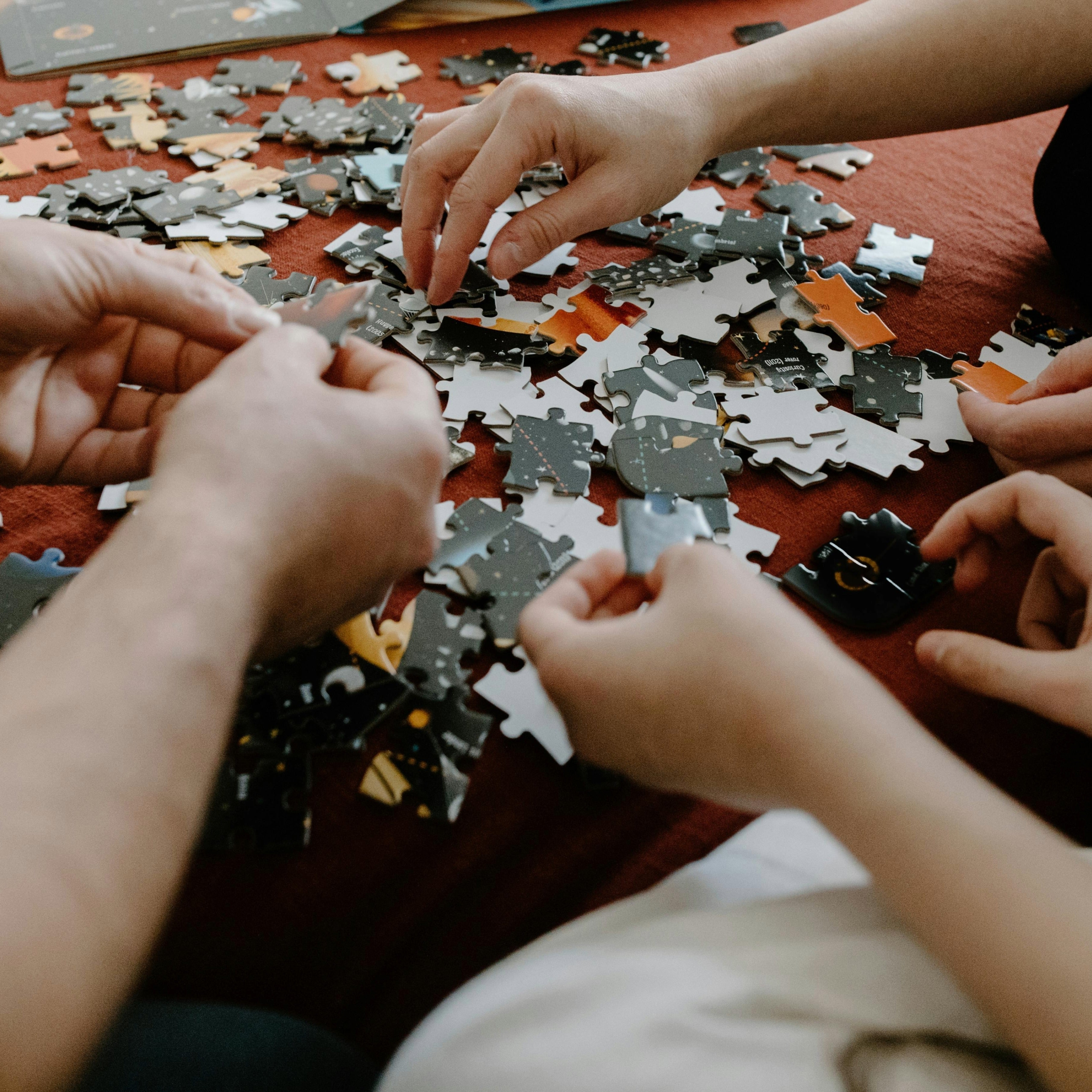 A close up of three people's hands assembling a puzzle